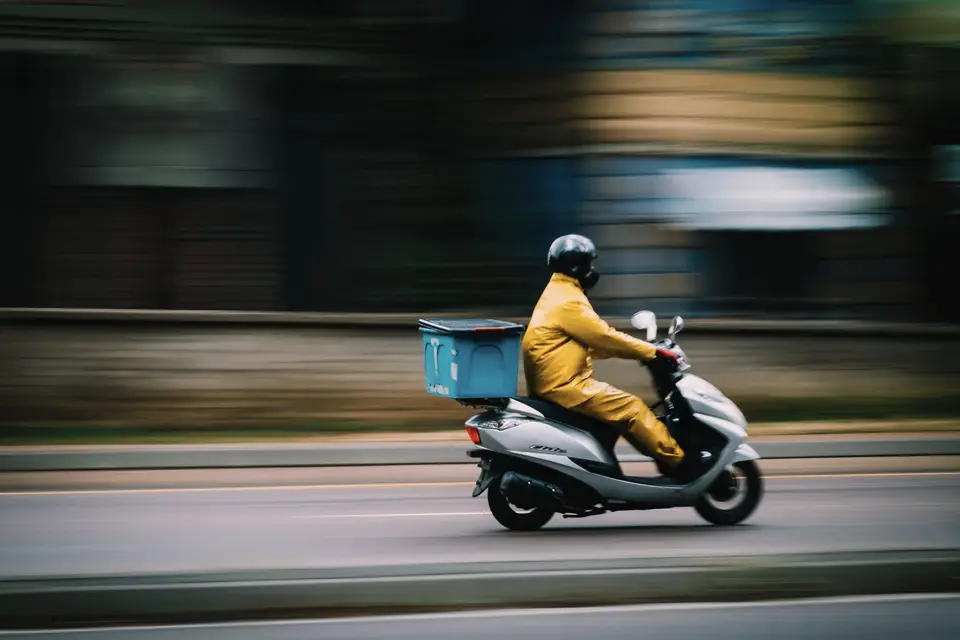 Teslimat kutulu scooter ile şehir içinde ilerleyen kurye
